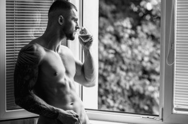 Yakışıklı kaslı adam yatak odasında pencere perdelerinde kahve içiyor. Genç yakışıklı seksi adam evde dinleniyor. Atletik kaslı bir adam. Yatak odasında seksi, genç, çıplak bir adam. Baştan çıkarıcı gay