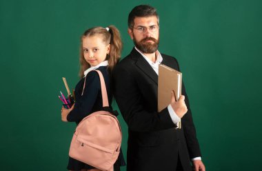 Okulda öğretmeni olan tatlı bir kız. Stüdyo portresi. Sırt çantası ve karatahta yeşili üzerine ders kitabı olan bir kız öğrenci.