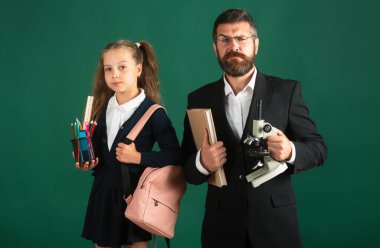 Ciddi bir öğretmen ve öğrencinin portresi okula hazır. Babamın portresi ve okul malzemeleriyle yeşil karatahta arka planda izole edilmiş küçük kızlar.