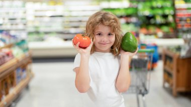 Çocuk gıda dükkanından meyve ve sebze seçiyor. Meyve ve sebze pazarındaki çocuklar. Satışlar, indirimler ve alışveriş. Tatlı çocuk sebze ve meyve tutuyor. Çocuk sebze ve meyve alışverişi