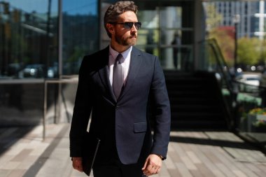 Modern ofis binasının önünde duran yaşlı bir iş adamı. İş başarısı. Dışarıyı düşünen bir iş adamı. Takım elbiseli modern iş adamı ofis manzarasının yanında duruyor.
