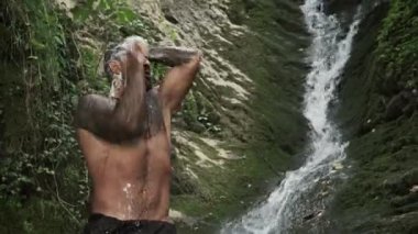 Attractive man having a shower in a tropical waterfall on summer vacations. Naked sexy man at a tropical waterfall, Bali. Man relaxing with freedom. Strong fit Man in waterfall in tropical nature