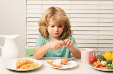 Çocuk yumurta yiyor. Çocuk portresi evde taze sağlıklı yiyecekler yiyor. Çocuk okuldan önce kahvaltı yapıyor.