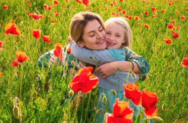Anne ve kızı gelincik çayırında sarılıyorlar. Anne ve kız gelincik çiçekleriyle tarlada dinleniyorlar. Kadın ve kız eğleniyor ve özgürlüğün tadını çıkarıyor.