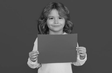 Kırmızı kağıt gösteren çocuk, sarı arka planda izole edilmiş. Elinde boş bir levha olan bir çocuğun portresi, poster. Mutlu çocuk, mutlu ve gülümseyen duygular