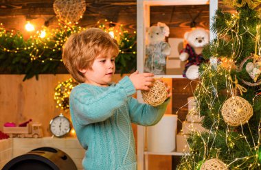 Noel ağacının yanında takı takan Noel elbiseli bir çocuk. Küçük oğlum Noel ağacını top ya da takı ile süslüyor. Mutlu küçük çocuk Noel ağacının önünde takı taşıyor.