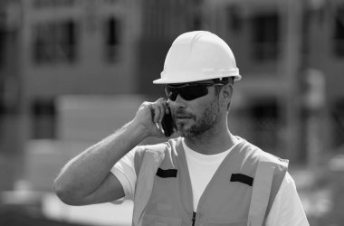 İnşaat alanında telefonu olan bir miğfer tamircisi. İnşaat mühendisi üniformalı inşaat mühendisi. Yeni bir ev inşa etmeye hazır inşaatçının portresi