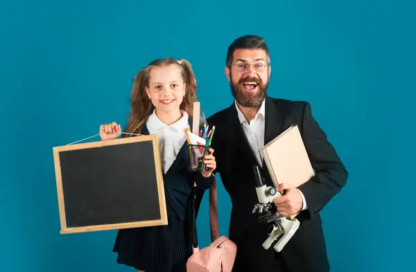 stock image Portrait of smiling teacher and happy pupil schoolgirl ready to school. Portrait of dad and little girls with school supplies, isolated on blue background