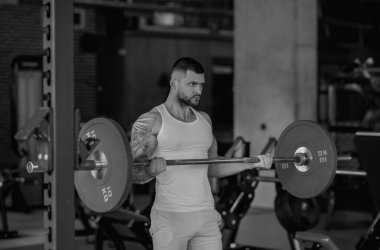Kas yığını adam spor salonunda dambıllarla antrenman yapıyor. Spor salonunda poz veren kaslı yakışıklı bir adam. Kas sporcusu dambılı kaldırıyor. Spor kulübünde esneme, spor egzersizleri.