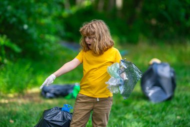 Lastik eldivenli çocuk çöp torbasıyla ormandaki çöpleri temizliyor. Eko, çevre koruma. Kirliliği geri dönüştür. Çocuk çöp ve plastik çöp topluyor. Çevreyi koru. Eko çocuklar