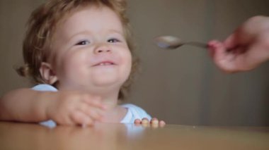 Sevimli bir bebek kaşıkla yemek yer. Çocuk maması yiyen aç küçük bir çocuk. Bebek yulaf lapası. Yemek zamanı. Küçük bebek sağlıklı yiyecekler yiyor. Küçük bir bebek yemeğini yiyor. Yiyeceği olan çocuğun yakın plan portresi