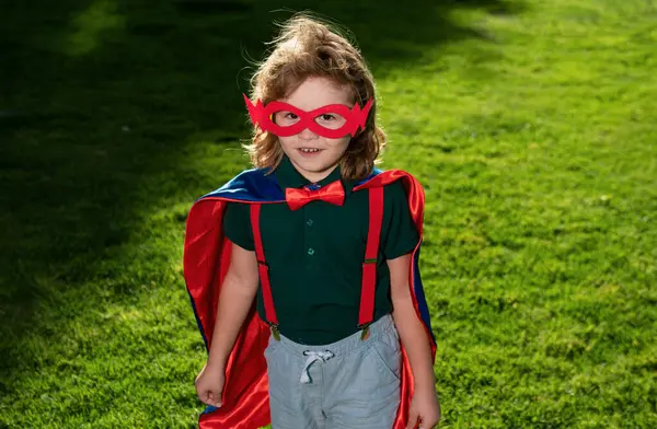 Yeşil çimlerde kırmızı pelerinli çocuk süper kahraman. Çocuk zaferi ve başarı kavramı