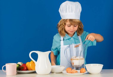 Aşçı önlüğü giymiş çocuk aşçı ve stüdyo arka planında izole edilmiş şef şapkası. Sağlıklı beslenme çocuklar için.