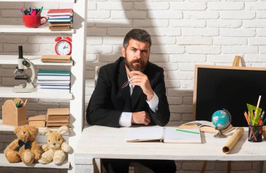 Anaokulundan erkek öğretmen portresi ya da sınıfta masa başında çalışan ilkokul. Olgun bir adam sınıfta oturmuş kameraya bakıyor.