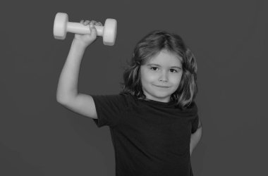 Dambılı spor çocuk portresi, sarı stüdyo arka planında izole edilmiş. Dambıllarla çalışan çocuk portresi. Çocuklar için motivasyon ve spor kavramı
