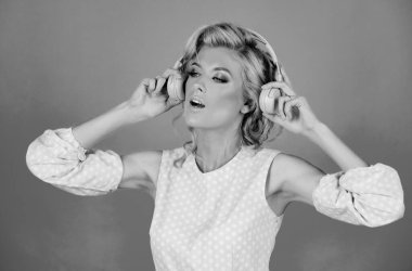 Image of blonde amazed woman listening to music with headphones isolated over studio background. Excited young girl with headphones listening to music and dancind