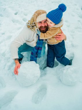 Baba ve çocuk gülümsüyor ve sarılıyorlar. Noel tatili ve baba ve oğul ile kış yeni yıl. Parkta soğuk güneşli kış havasında baba ve oğulun dış portresi