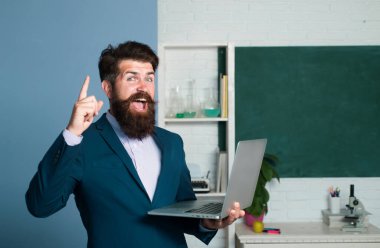 Dizüstü bilgisayarlı öğretmenin bir fikri var. Öğrencileri bekleyen hayret verici öğretmen, özgüvenle gülümsüyor. Pozitif ifade duyguları komik yüz