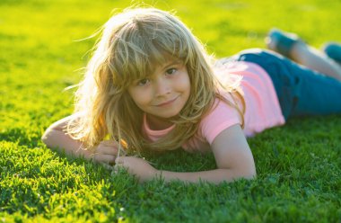 Bahar çocuğu suratı. Çimen geçmişi olan gülümseyen çocuk. Mutlu küçük çocuk bahar günü çimlerin üzerinde yatıyor. Parktaki yeşil çimlerde yatan gülümseyen bir çocuğun portresi