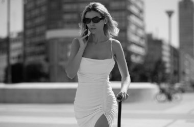 Tatile giden telefon valizli modacı kadın. Seyahat yaşam tarzı. İş gezisindeki seksi genç kız sokakta bavulla yürüyor.