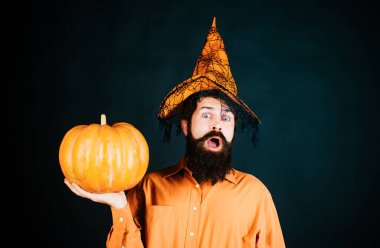 İzole edilmiş arka planda balkabağı olan yakışıklı bir adam portresi. Cadı şapkalı sakallı cadılar bayramı adamı. Stüdyo yakın çekim. Şükran Günü mevsimsel yemek malzemeleri.