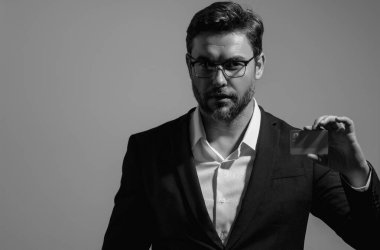 Elinde kredi kartı tutan yakışıklı bir adam. Gri stüdyo geçmişinde kredi kartı olan orta yaşlı bir adam. Kredi kartı konsepti. Takım elbiseli bir işadamı kredi kartıyla ödeme yapıyor.