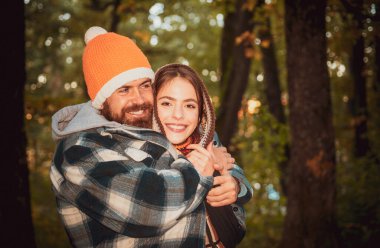 Mutlu gülümseyen ve sıcak örgü şapkalı ve eşarplı çiftler sonbahar ormanlarında dışarıda yürüyorlar. Sıcak hava ve sonbahar ilham konsepti. Düşen sarı ağaçlar arka plan