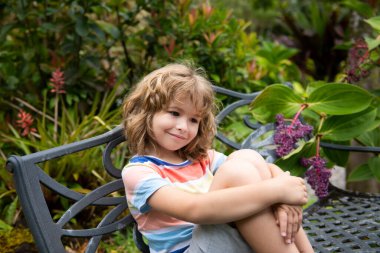 Çocuk bankta oturur. Çocuklar yüzlerini kapatıyorlar. Komik çocukların açık havada çekilmiş hayat tarzı yakın plan portresi. Yazlık çocuk açık hava portresi. Şirin çocuğun yüzünü kapat.