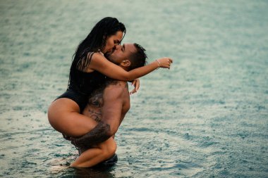 Yaz modelleri. Sevgi dolu bir çift. Birbirine aşık yaz çifti. Yazın denizde tatil yapan, aşık seksi bir çift. Tutkulu çift deniz suyunda öpüşüyor ve sarılıyor. Yaz aşıkları