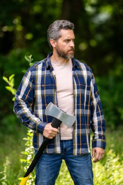 Ciddi yüzlü oduncu dışarıda balta taşıyor. Ormanda baltayla kereste işçisi. Ekose gömlekli, baltalı, güçlü bir oduncu. Oduncu ya da ormandaki oduncu