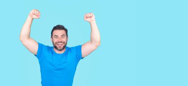 Kazanan. Başarılı bir adam kollarını kaldırdı. Kollarını kaldırıp başarıyı kutlayan heyecanlı adam. Mavi arka planda izole edilmiş heyecanlı bir erkek modelin portresi. Kutlama yapan adam kazanır. Başarı. Heyecanlı kazanan