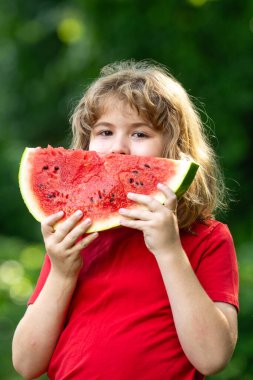 Kid 'in karpuzlu yaz portresi. Yazlık parkta karpuz yiyen komik çocuk. Bahçede karpuz yiyen bir çocuk. Çocuklar dışarıda meyve yer. Çocuk karpuz seviyor.