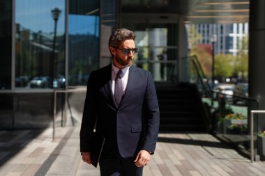 Modern ofis binasının önünde duran yakışıklı bir milenyum işadamı. İş başarısı. Dışarıyı düşünen bir iş adamı. Takım elbiseli modern iş adamı ofis manzarasının yanında duruyor.