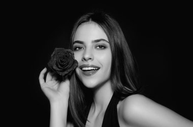 Rose 'u tutan genç kadın. Yüzünde kırmızı gül olan güzel kız. Stüdyo çekimi. Romantik seksi kadın. Doğum günü ya da Sevgililer Günü için çiçekler, siyah stüdyo geçmişi