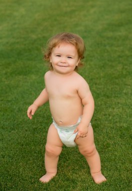 Çocuk, bez takmış komik bir bebek yeşil çimlerde oynuyor, yaz aylarında açık havada çocuk hayatı sürüyor.