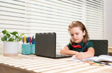 Küçük öğrenci ödevini evde bir tablet ya da dizüstü bilgisayarla yapıyor. Öğrenci görevi bir deftere yazar. Akıllı çocuklar için eğitim ve öğrenim, evde eğitim