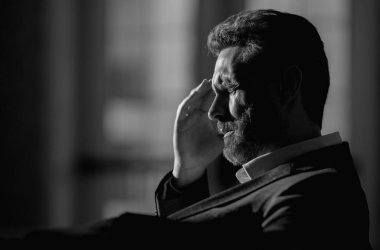 Baş ağrısı çeken yorgun bir adam. Başa dokunmak, ağrıyı dindirmek, migren. İş sorunları. İflas, mali sorun ve kriz konsepti. Bin yıllık İspanyol adamın başı ağrıyor. Migren.