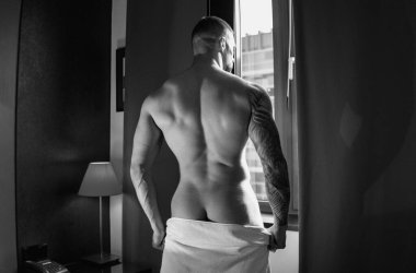 Sensual muscular hunk in room on window curtains. Muscular shirtless man model in bedroom. Gay sexy model. Strong shoulders and chest. Muscular sexy man with naked torso. Hunk with athletic body
