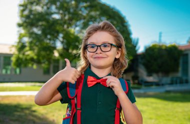 Happy smiling schoolboy pupil in glasses with thumb up is going to school. Kid outdoors of the school clipart