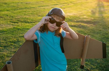 Sırt çantalı kanatlı çocuk gezgin. Pilot pilotculuk oynayan sevimli çocuk ve dışarıda parkta hayaller kuruyor.