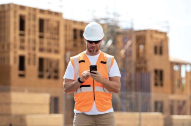 Worker man on the building construction. Worker using phone, builder chatting on phone a break from work. Architect with mobile phone. Construction site worker outdoor portrait