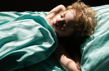 Sakin bir çocuk rahat bir yatakta uyur yumuşak bir yastıkta yatar ortopedik yatakta, güzel bir çocuk battaniyeye sarınır yatak odasında, üst manzara