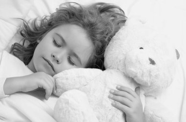 Little boy sleeps. Cute child sleeping with a toy teddy bear on bed at home. Bedtime, kid sleeps. Kid asleep on soft pillow with blanket having healthy sleep