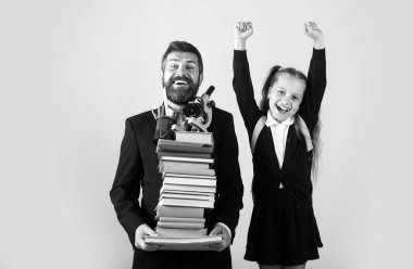 Cheerful smiling little girl in school uniform having fun in classroom. Fun kids education. Father or teacher hold big stack school textbook notebook book, isolated. Kids education concept
