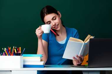 Öğrenci sınıfta kahve içiyor. Üniversitede kahve molası. Öğrenci kız kahve fincanı tutuyor. Lisedeki bilgi. Lise ya da üniversite konsepti. Genç üniversite öğrencisi tahtanın yanında çalışıyor.