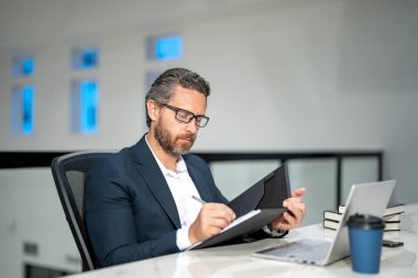 Ofisinde dizüstü bilgisayarı olan bir iş adamı. Modern ofiste çalışan uzaktan kumandalı personel. İş adamı çevrimiçi toplantıda. İnternette çalışan İspanyol iş adamı. İş yerinde laptop kullanan olgun bir iş adamı