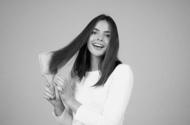 Beautiful model girl with comb brushing hair. Beauty woman with straight hair on studio background. Woman holding hairbrush near face. Healthy hair. Hairstyle and hair care concept. Shiny hairs