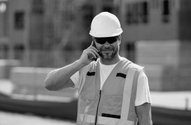 Çalışanlar telefon kullanıyor, inşaatçılar işe ara veriyor. Cep telefonu olan bir mimar. Kasklı inşaat işçisi dışarıda çalışıyor. Binalarda güvenlik kaskı takan bir inşaatçı.