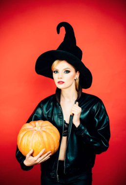 Siyah cadı cadılar bayramı kostümlü genç kadınlar kırmızı arka planda parti veriyorlar. Cadı balkabağıyla poz veriyor