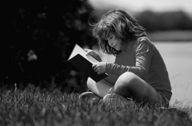 Akıllı çocuk dışarıda parkta kitap okuyor. Yazın kitap okuyan sarışın çocuk. Zeki çocuklar açık hava portresi. Çocukların hayal gücü, yenilik ve ilham kaynağı. Açık okul, öğrenen çocuklar.